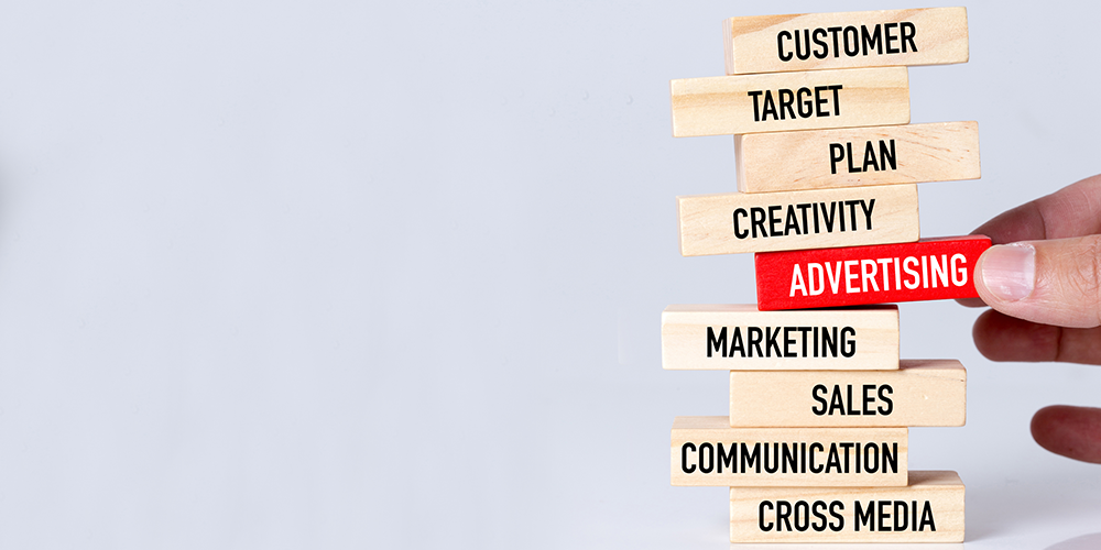 Hand sets Advertising piece into a Jenga-like puzzle with other ad buzz words.