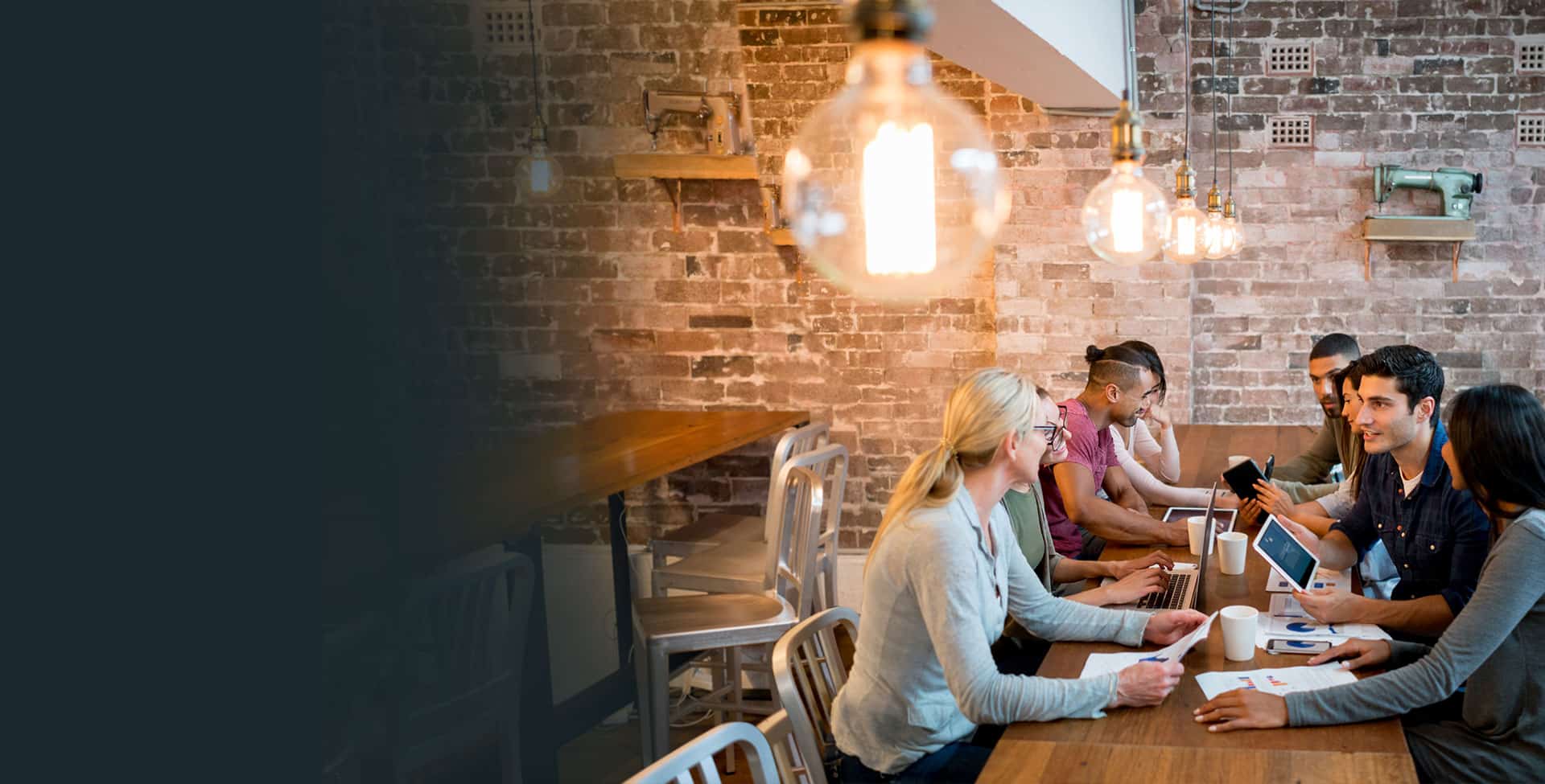 Eight coworkers, four male and four female, smile and gather at a café to discuss their work.