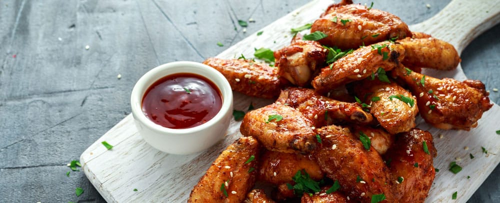 Platter of buffalo wings with dipping sauce is delivered to gray, concrete table.