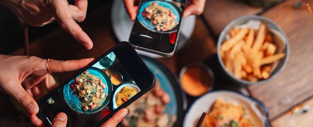 Friends hold their phones over their meals to take pictures and post them in social media.