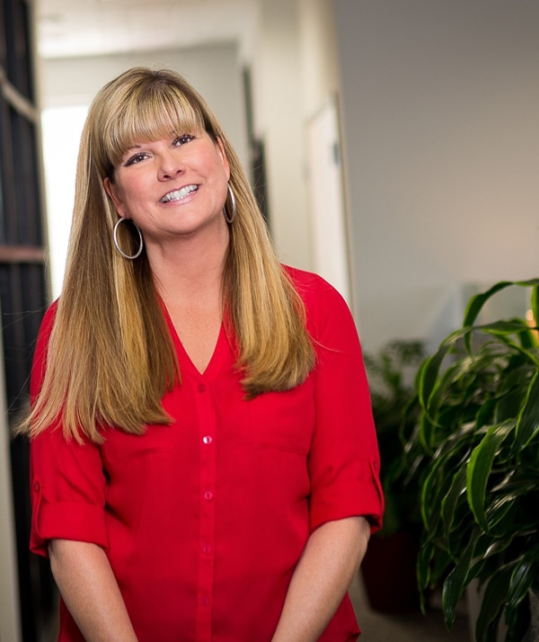 SAUCE Owner and President Tina Myszewski smiles for camera in office with plant in background.